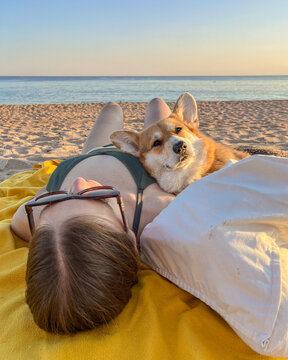 Woman relaxing on beach with corgi dog at sunset