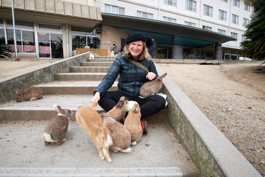 Tourist on Rabbit Island sitting on floor with wild rabbits feeding