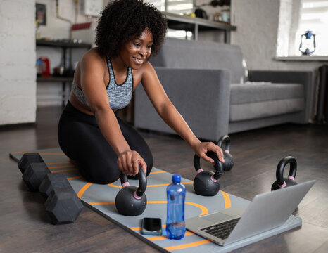 Happy black sportswoman with kettlebells and laptop