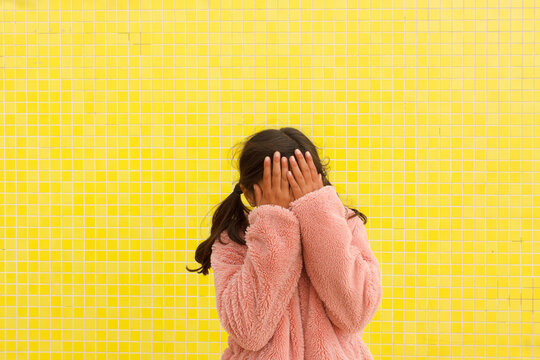 Girl Covers Her Face in Front of Yellow Wall 