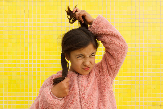 Child Pulls Hair While Making Funny Face Against Yellow Background