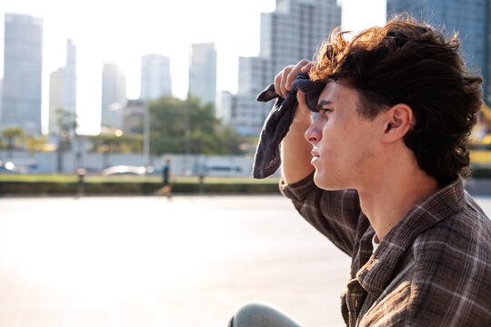 Man applying wet towel to forehead in extreme heat with city skyline