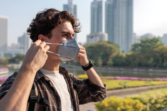 Man adjusting face mask in city park during warm weather