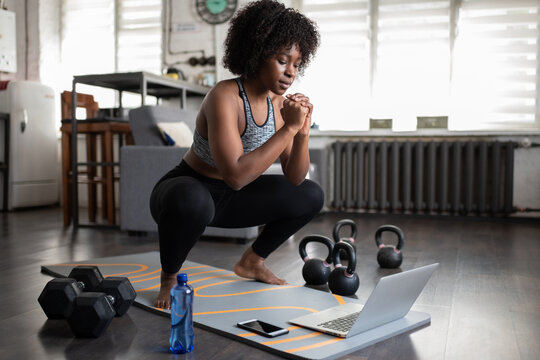 African American sportswoman squatting during online workout