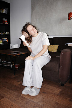 Person drying curly hair on sofa at home