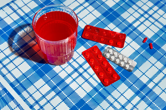 Red drink, pills and blister packs on blue checkered background