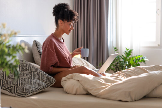 Woman in bed with laptop and coffee.