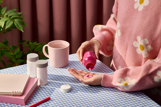 Woman in floral sweater pouring pink pills from bottle into her hand