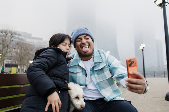Father and daughter making funny faces taking selfie with dog