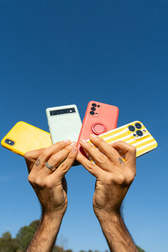Hands holding multiple phones blue sky