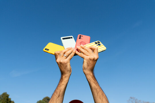 Hands holding multiple phones blue sky