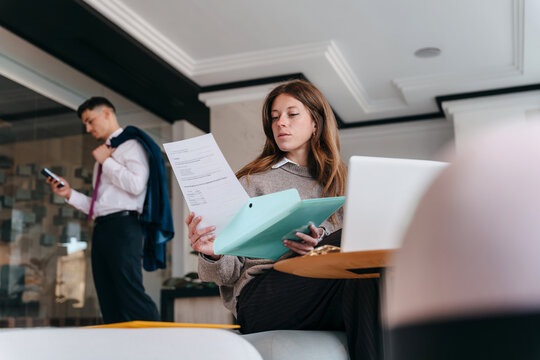 Woman Reviewing Documents While Man Uses a Phone in Office