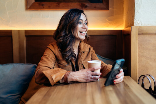 Happy woman laughing drinking coffee using phone