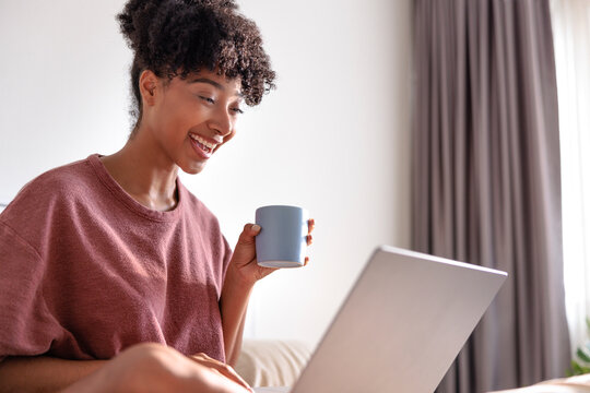 Woman smiles, works on laptop, and holds a coffee mug
