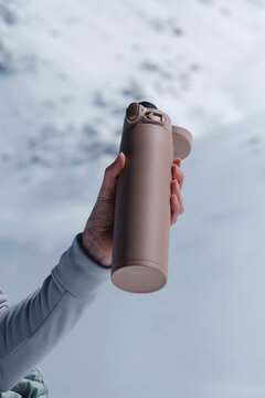 Hand holding thermos against sky and snow.