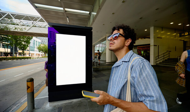 Man checking phone near digital billboard at bus stop