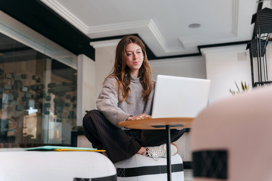 Woman Works on Laptop While Sitting on a Stool in a Modern Office