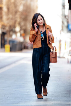 Woman walking on street talking on phone smiling