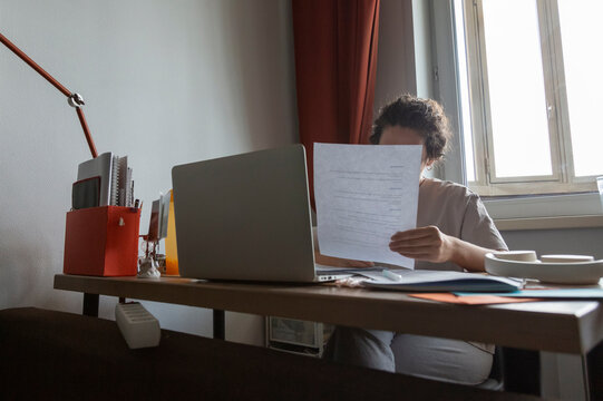 Person studying paperwork at desk with laptop