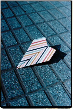 close-up of a paper airplane on textured paving stones, 35mm film