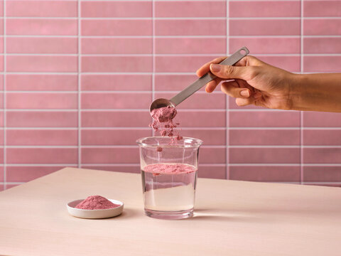 Hand adding pink powder supplement to glass of water