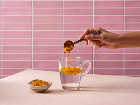 Adding turmeric powder from a spoon into a glass of water