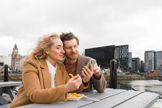Couple Enjoys Fries And Use Cellphone At Liverpool Waterfront