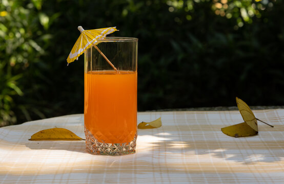 Summer drink served in a glass with a decorative cocktail umbrella on a table, with nature in the background. Concept of vacation, freshness, relaxation, and outdoor enjoyment