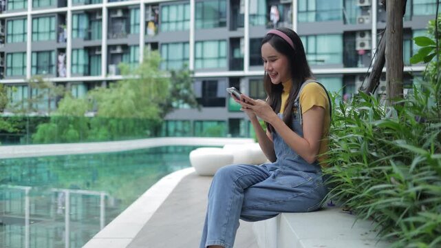 Beautiful girl relaxing with a phone at a modern apartment garden and pool. Professional shot for real estate and leisure living themes.