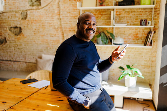 Smiling man working with mobile phone in sunlit office