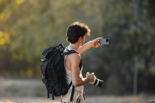 Male photographer holding smartphone and camera outdoors