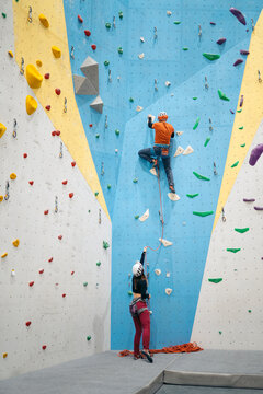 Climber ascending indoor rock wall with belayer helping