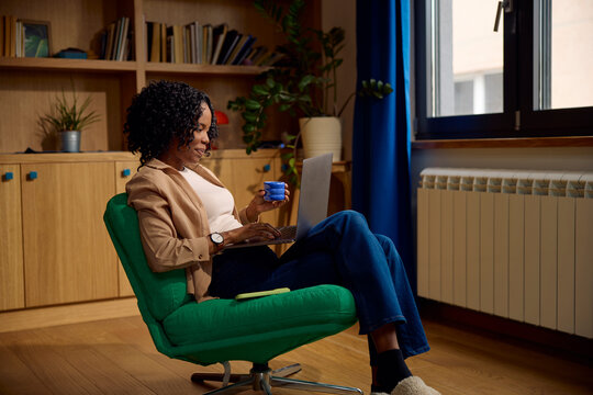 Woman uses her laptop while seated in a green chair by the window