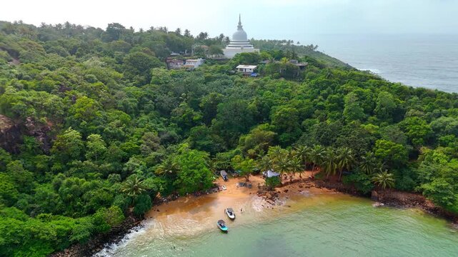 Aerial view of Jungle Beach and the Japanese Peace Pagoda surrounded by lush tropical forest and the ocean in Southern Province, Sri Lanka.