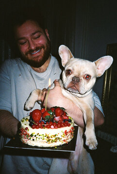 Man holding French bulldog and birthday cake indoors