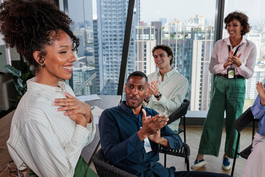 Diverse team applauds woman in modern office setting.