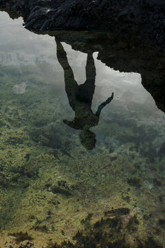 Reflections of a person in clear water near a rocky surface