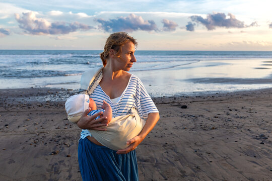 Mother Carrying Baby in Sling on Beach at Sunset