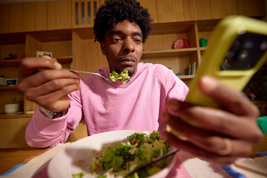Mman eats at home engrossed in his phone