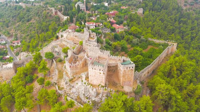Alanya, Turkey. Ehmedek Castle, a medieval stone fortress with crenellated towers and fortified walls, aerial view over dense green forest on a mountain slope in summer. Aerial View, MasterShots, Roc
