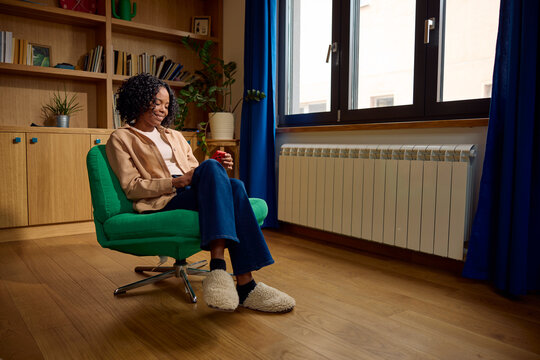 Woman sits in a green chair and uses her phone.