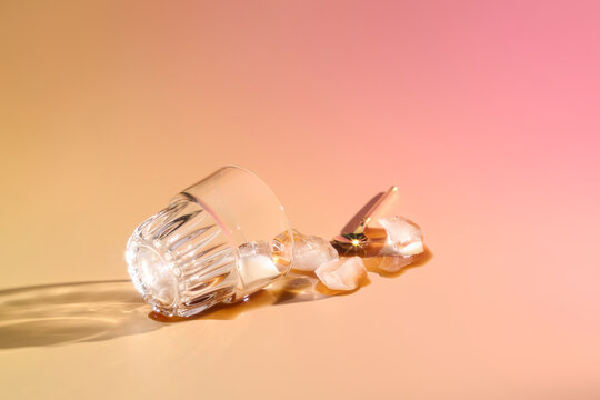 Spilled glass with ice cubes and a golden spoon on soft pink