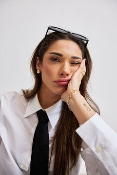 Woman sits with hand on face while wearing a white shirt and tie