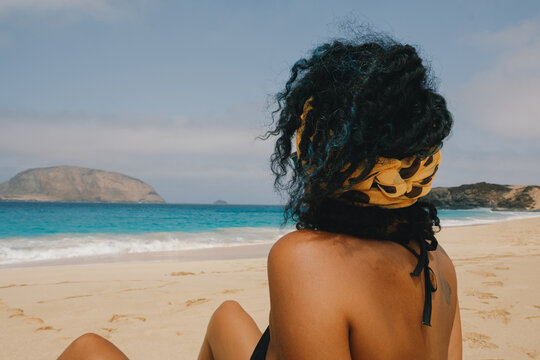 Woman sits on beach and enjoys view of ocean and island