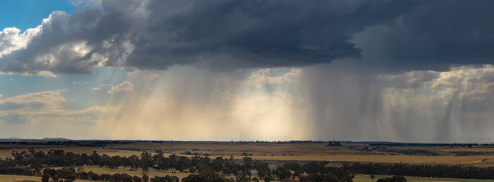 Heavy rain falling from a dramatic storm clouds over dry farmland