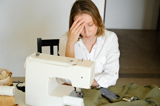 A woman stressing and sitting close to a sewing machine.
