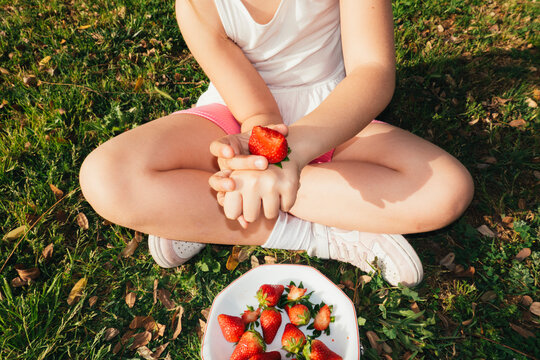 Hand holding strawberry with bowl of fruit outdoors

