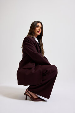 Business woman poses in suit with heels on simple background