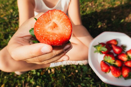 Hand holding strawberry with bowl of fruit outdoors
