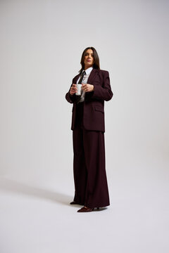 Person standing in a suit holding a cup in a simple studio setti